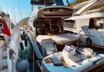 Large luxury motor yacht docked between smaller boats in a marina, with a white inflatable tender in front of the stern.