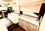 Luxurious motorhome interior with a white sofa, wood cabinetry, and large side windows with pink-tinted blinds in the background.