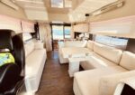 Cream-toned yacht salon with an L-shaped sofa, central white table, and large windows looking out to the water.