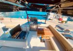 Cockpit of a luxury boat with a wooden folding table, seating, grill, and a marina with boats in the background.