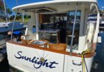 Back view of a white motorboat named Sunlight, with wooden seating, a round table, and an open rear deck at a marina.