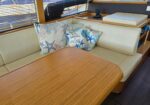 Cream-colored booth seating around a polished wooden table in a nautical yacht interior, with beach-themed pillows nearby.