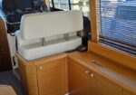 Wood-paneled yacht cabin with captain's chair facing navigation panel and helm controls, overlooking a marina through a window with blinds.