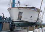 White motor yacht on a boat lift at a marina dry dock, with blue crane equipment in the background.
