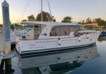 White motor yacht named 'GREENLINE 40' docked at a marina, calm water reflecting the boat and surroundings.