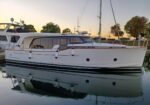 White motor yacht moored in calm water at sunset, with fenders along the hull and a reflection visible in the water (name Greenline 40)