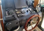 Boat helm with wooden steering wheel, Raymarine navigation screens, and control panels on a yacht cockpit