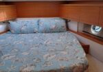 Boat cabin bedroom with a queen bed, shell-pattern quilt, and built-in wooden storage along the walls.