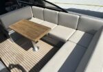L-shaped beige cushioned seating around a wooden rectangular table on a boat deck with teak flooring.