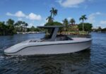 White motorboat with a black T-top gliding on a calm waterway, palm trees and waterfront homes in the background.