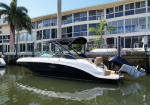 White and black speedboat moored at a dock along a canal, with a black canopy and beige seating, and a modern glass-front house in the background.