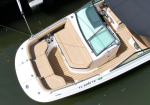 Top-down view of a white motorboat with beige cushioned seating and a teak-deck cockpit docked in calm water.