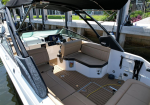 Brokered view of a tan-cushioned boat cockpit with steering wheel and dashboard under a black bimini, at a dock.