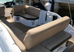 Tan cushioned U-shaped seating area in a white motorboat with a teak-like deck and beige upholstery.