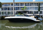 White and black speedboat moored at a dock in front of a modern glass-front house with palm trees in the background.