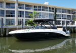 White and black motorboat moored at a dock along a canal with a glass-front building in the background on a sunny day.