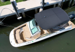 Top-down view of a white motorboat docked at a pier with tan seating and a black canopy.