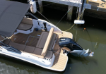 Top-down view of a white motorboat docked at a pier, featuring tan seating, a wood-style deck, and a large outboard engine at the stern