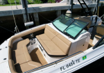 A beige-cushioned boat cockpit with wraparound seating and a glass windshield, docked at a marina, Florida registration visible on the hull (FL 6484 TE).