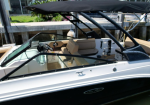 White and black speedboat interior with beige seating and a canopy, docked by a wooden pier