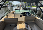 Open-cockpit boat interior with beige seats, wooden deck, and a steering wheel facing the dashboard, docked along a canal.