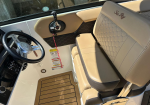 Interior helm of a Sea Ray boat with beige captain's seat, black steering wheel, and control panel to the left; sunlit cockpit.