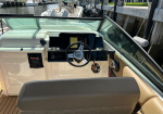 Boat cockpit at the bow showing steering wheel, touchscreen displays, and beige seating, docked at a marina.