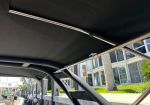 Interior view of a black boat canopy frame with chrome supports and ties, moored by a marina side in the background