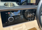 Close-up of a boat dashboard showing a Fusion stereo with a large volume knob, a red HORN button, and labeled controls (NAV, ANCHOR, COCKPIT) for lights and vessel functions; steering wheel to the right and a cup holder above.