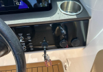 Close-up of a boat helm: ignition switch with key inserted, several circular controls, and a cup holder above on the console