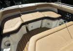 Tan cushioned boat seating around a U-shaped cockpit with a tan deck, water visible beyond the railings, and a built-in cooler underneath the seat.