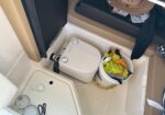 Compact boat head with a portable toilet and a white bucket filled with colorful towels beside it.