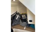 Small storage nook with black-and-white patterned pillows, a striped bag, and a few items tucked beside a cabinet on a boat or camper interior.