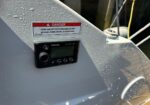 Marine boat deck showing a Fusion MS-NRX300 marine stereo mounted on a gray surface with water droplets; warning label nearby.