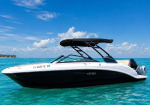White and black speedboat with a dark canopy on calm turquoise water under a bright blue sky with scattered clouds, side view.