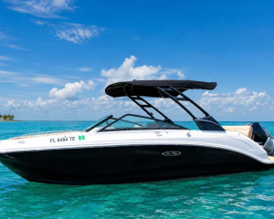 White and black speedboat with a dark canopy on calm turquoise water under a bright blue sky with scattered clouds, side view.