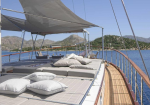Sun loungers with cushions on a luxury yacht deck, blue sea and distant rocky islands in the background under a clear sky.