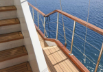 Wooden yacht stairs with a metal railing, leading to a deck beside blue water.