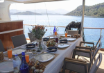 Dining table set for a meal on a yacht, with a floral centerpiece and sea view beyond the deck railing.