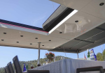 Outdoor yacht dining area with a skylight, white tablecloth, wine glasses, bottles, and a flower centerpiece, hillside in background.