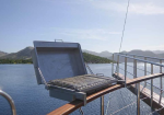 Metal grill mounted on a wooden railing over blue sea with distant mountains in the background.