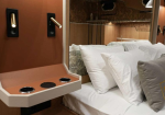 Hotel bedroom with a bedside alcove featuring cup holders and a small countertop next to the bed with white pillows and gray accents.
