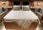 Luxurious yacht cabin with a large bed, gray pillows, and a white throw, flanked by wood-paneled walls and cushioned benches with colorful pillows on both sides.