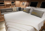 Luxurious yacht cabin with a king bed, white linens, beige throw, and built-in seating along a wood-paneled wall.