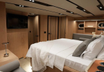 Luxurious yacht cabin with a large bed, white linens, gray pillows, wood paneling, built-in shelves, and a wall-mounted TV.