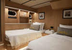 Twin-berth yacht cabin with white bedding and decorative gray pillows reading MOTO, wood paneling, and warm lighting.