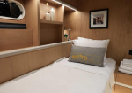 Wood-paneled cabin bedroom with a single bed, white bedding, and a gray accent pillow with gold lettering on a yacht-like interior.