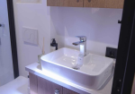 Modern bathroom sink with square white basin and chrome faucet, wood vanity, and nearby glass shower enclosure.