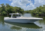 White motorboat with open bow and cabin, anchored on a calm waterway bordered by mangroves.