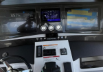 Boat cockpit console with multiple displays: left engine/monitor, center gauges, and right navigation/chart plotter; throttle and switches below the dash.